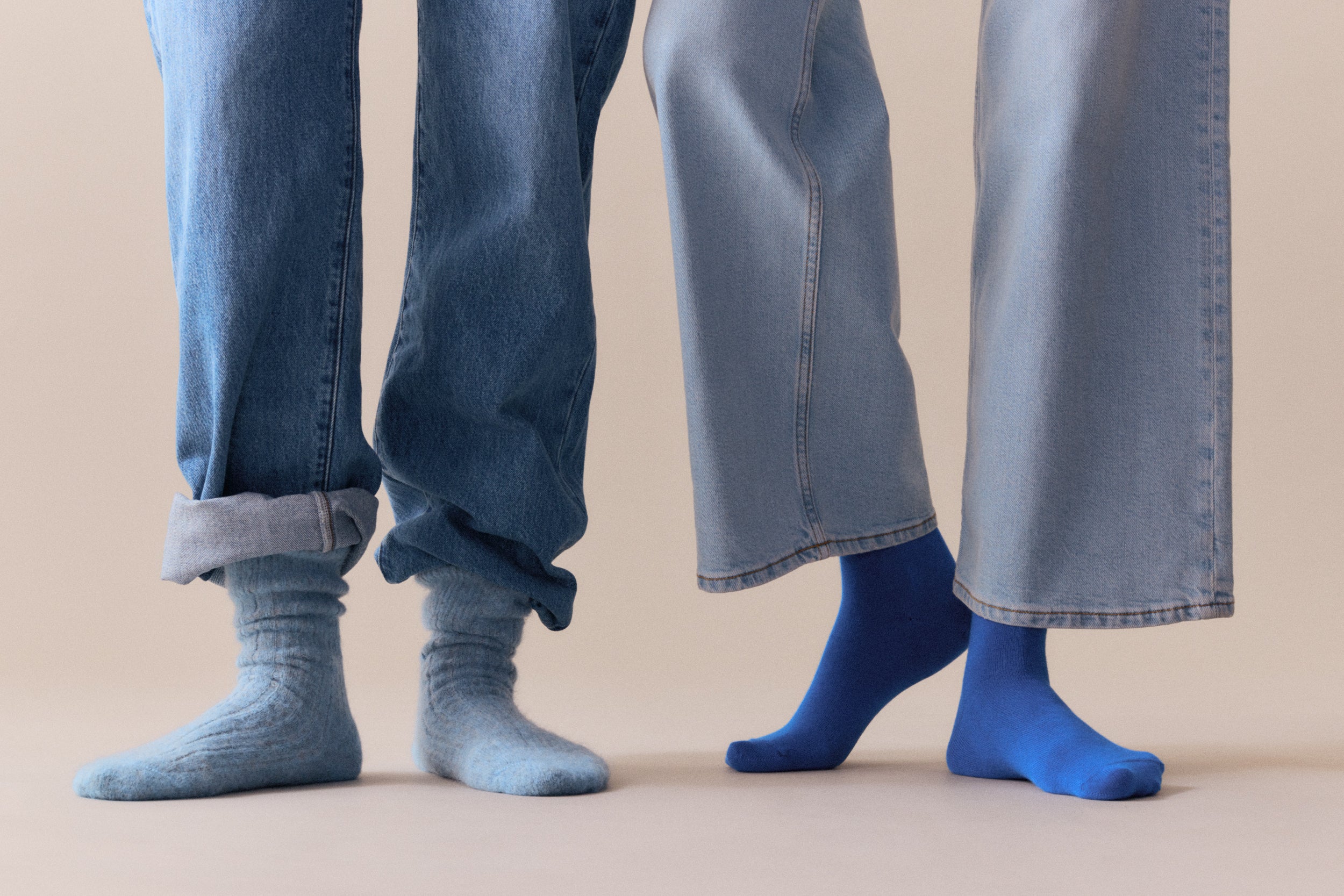 Two pairs of legs wearing jeans and socks on a beige background