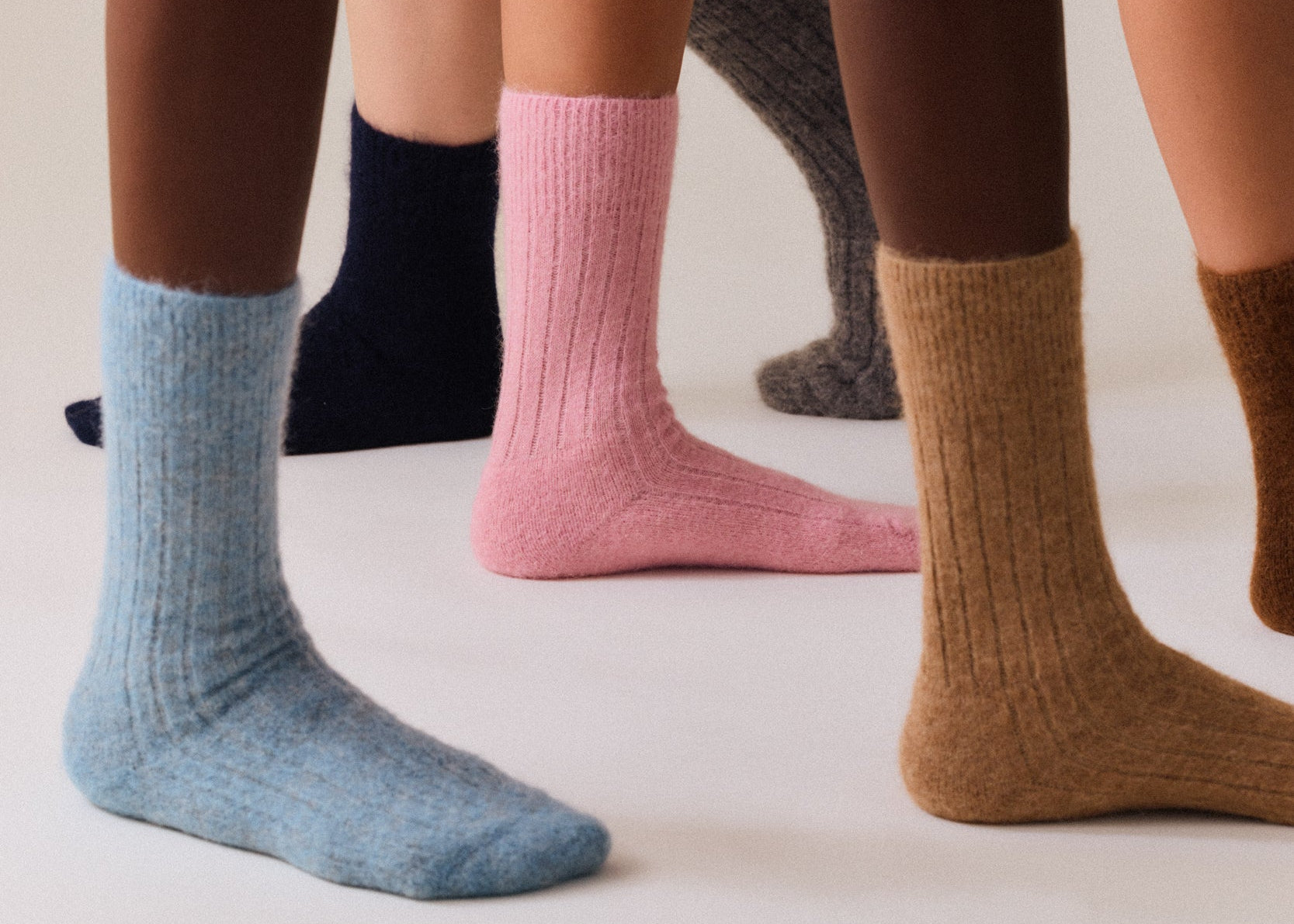 Four pairs of ultra soft socks in different colors worn by people on a neutral background