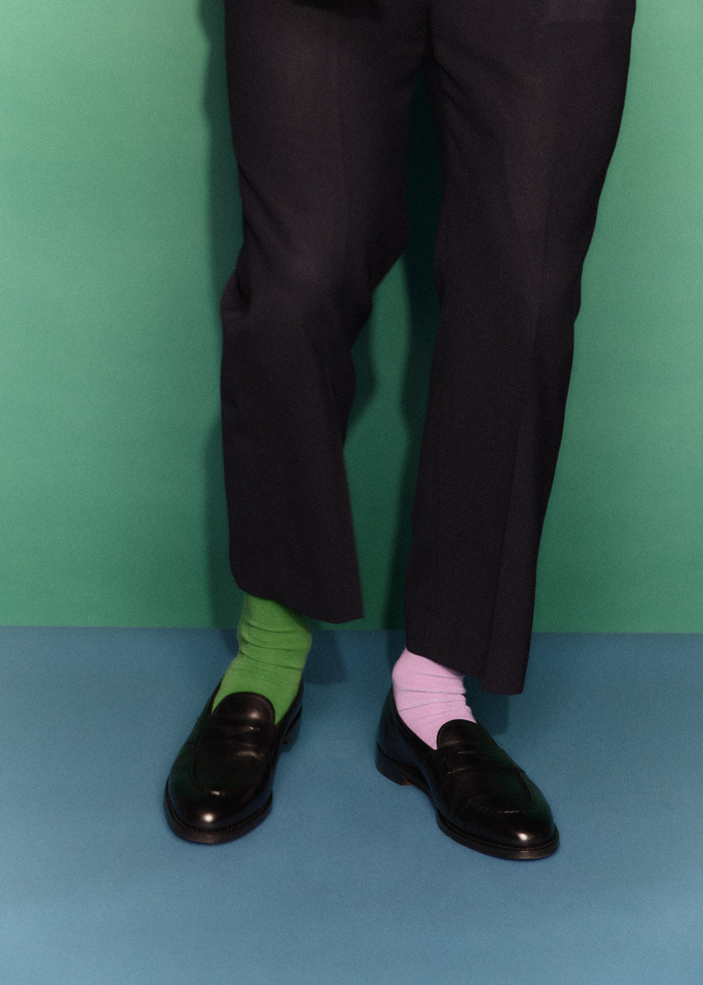 Person wearing black shoes, green socks, and pink socks against a green and blue gradient background