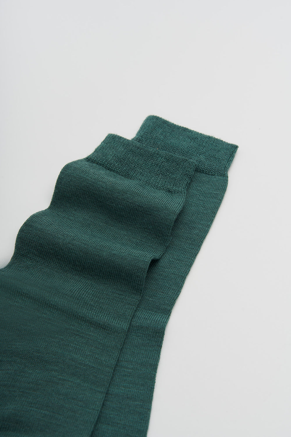 Pine green merino socks on a light grey background