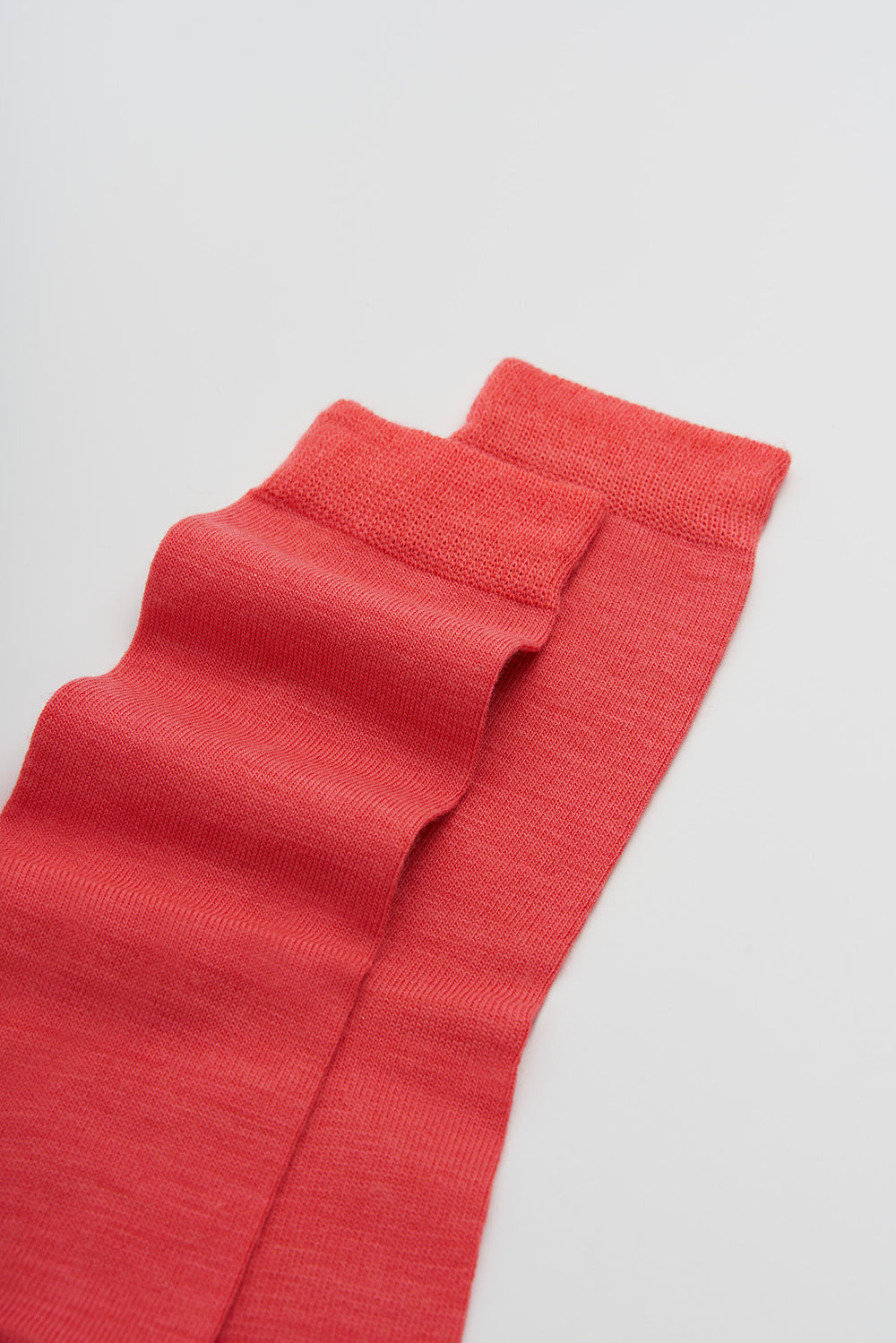 Coral red merino socks on a light grey background