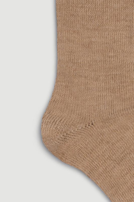 Close-up of the heel of a beige calf length alpaca sock on a light grey background