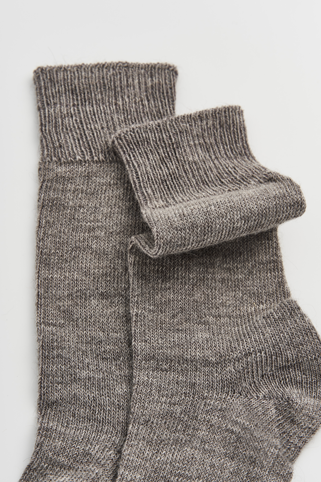 Close-up of the top of a pair of grey calf-length alpaca socks on a light grey background