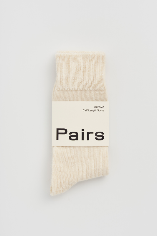 Pair of cream calf-length alpaca socks with a 'Pairs' packaging band on a light grey background