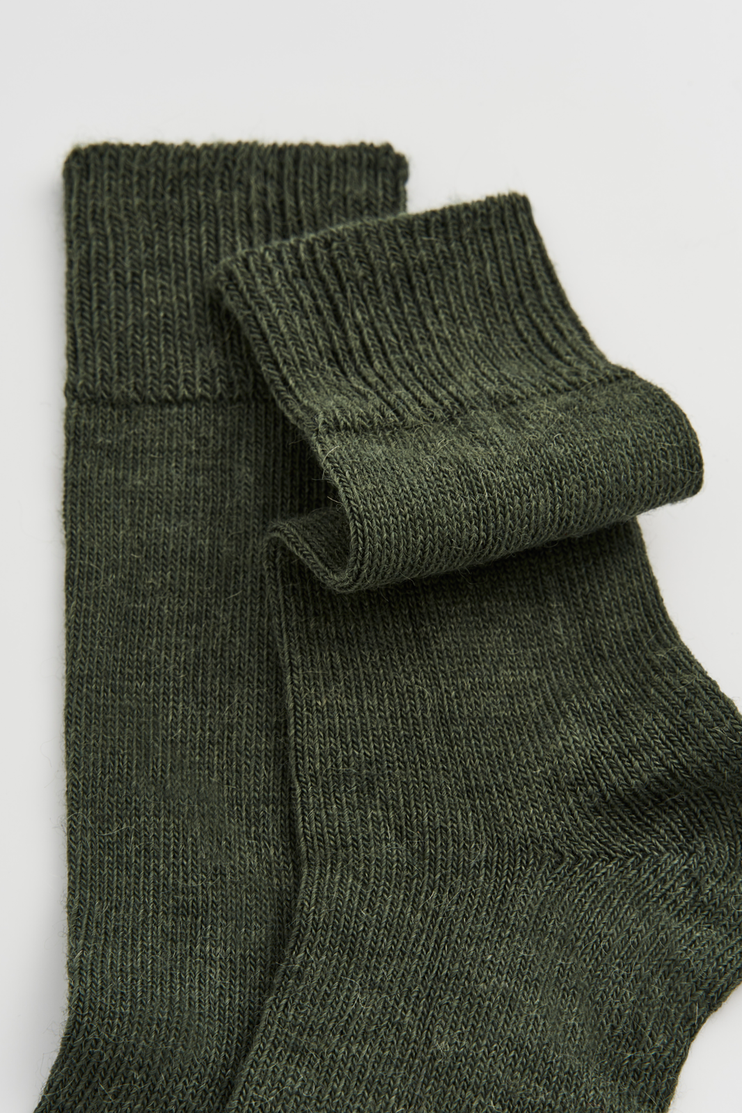 Close-up of a pair of green calf-length alpaca socks on a light grey background