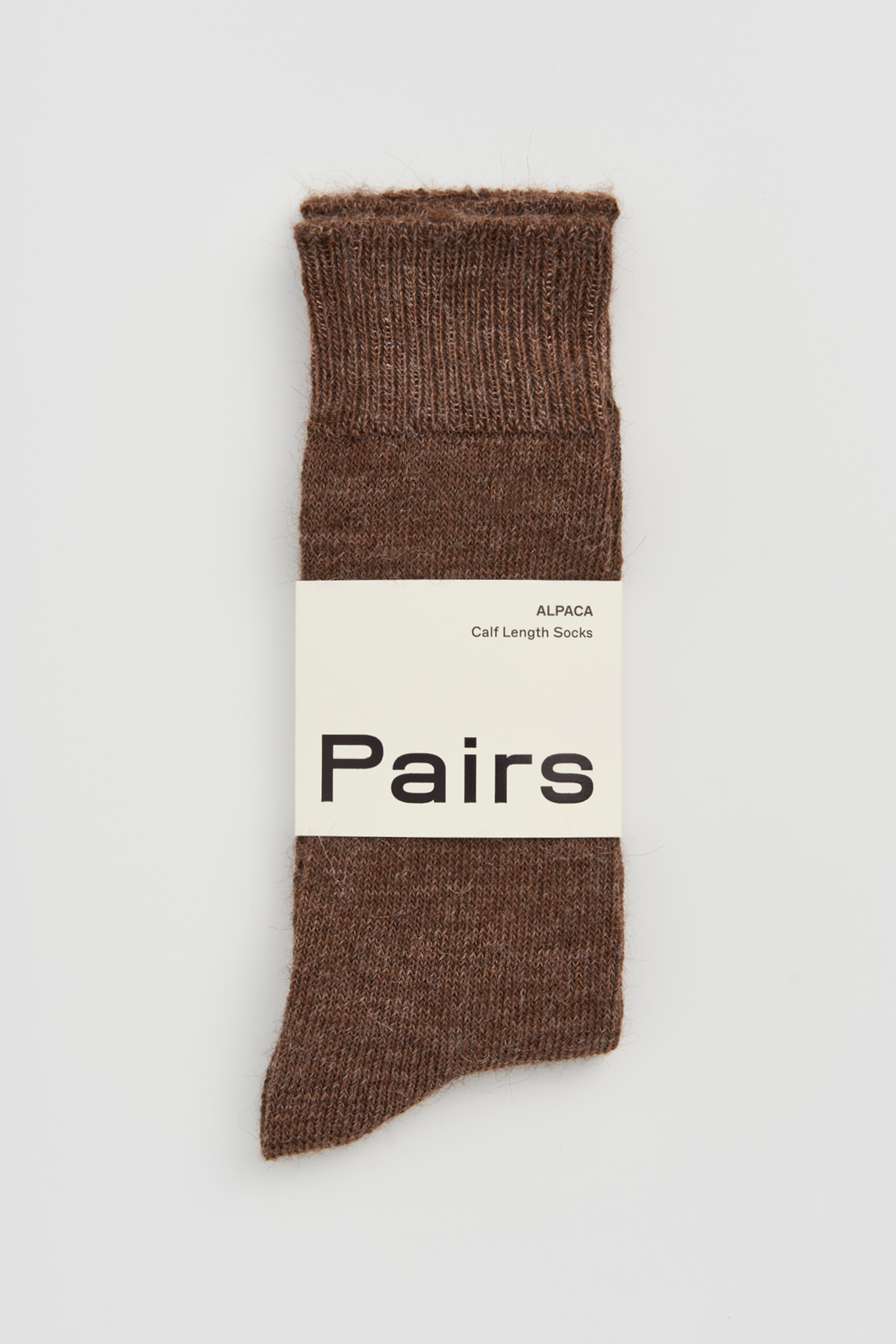 Pair of mid-brown calf-length alpaca socks with a 'Pairs' packaging band on a light grey background