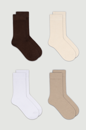 Four pairs of calf length bamboo socks in brown, cream, white, and beige on a light grey background