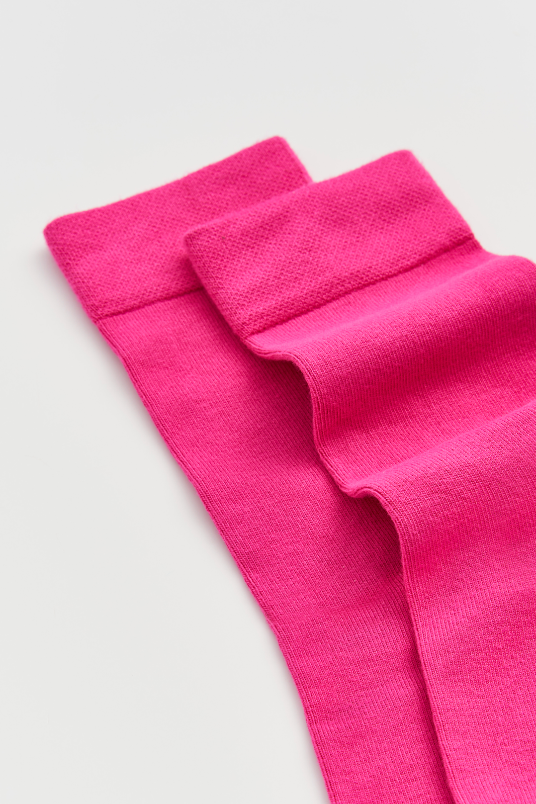 Close-up of the top of a pair of bright pink calf-length bamboo socks on a light grey background