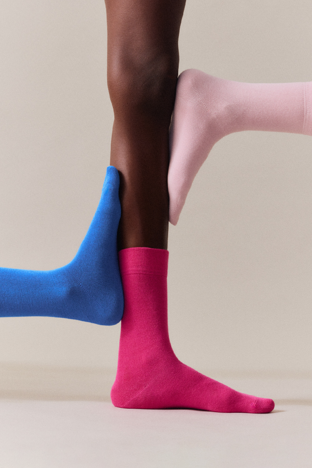 Three people wearing colourful  calf-length bamboo socks on a neutral background