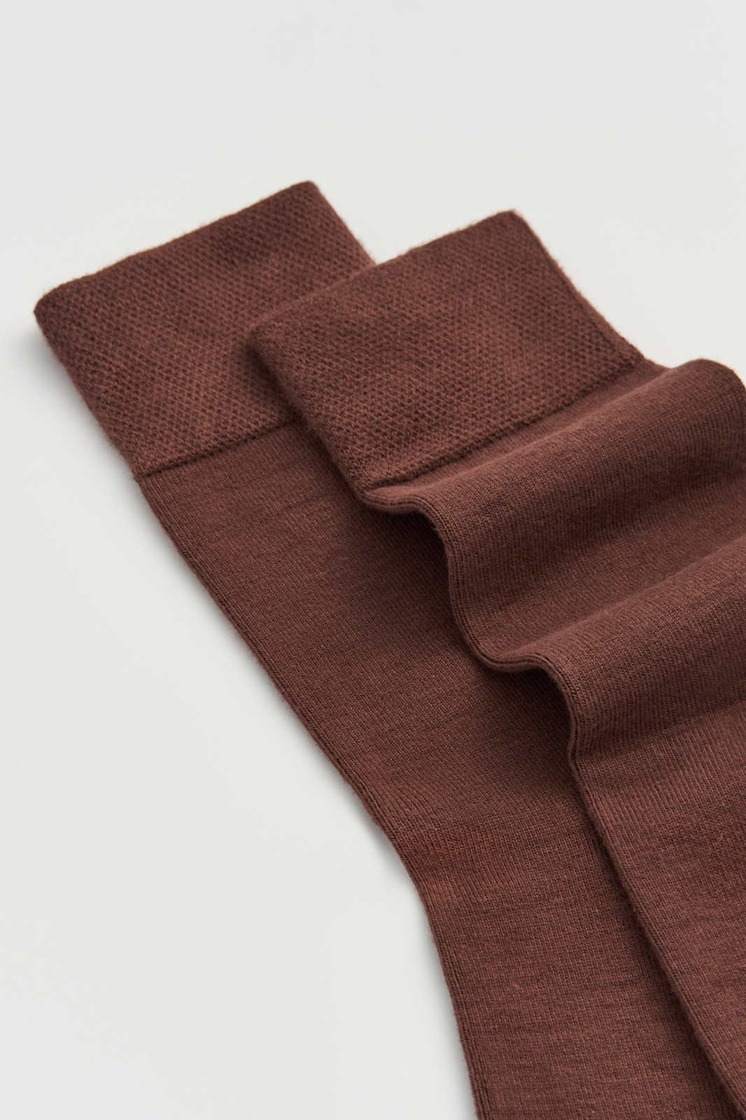 Close-up of the top of a pair of brown calf-length bamboo socks on a light grey background