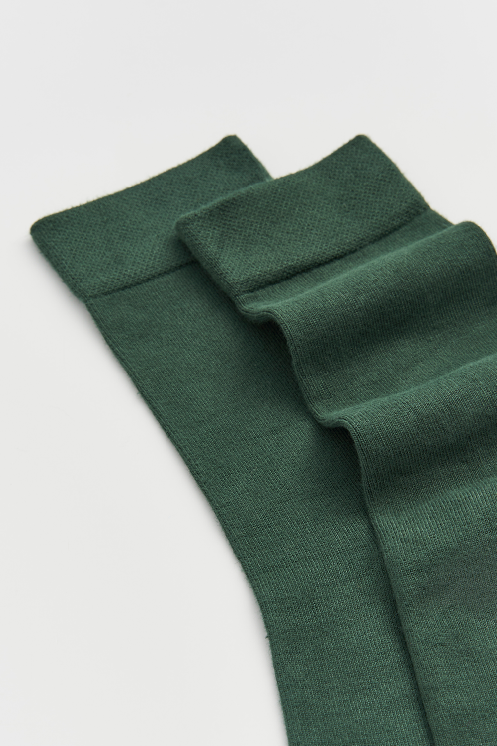Close-up of the top of a pair of green calf-length bamboo socks on a light grey background