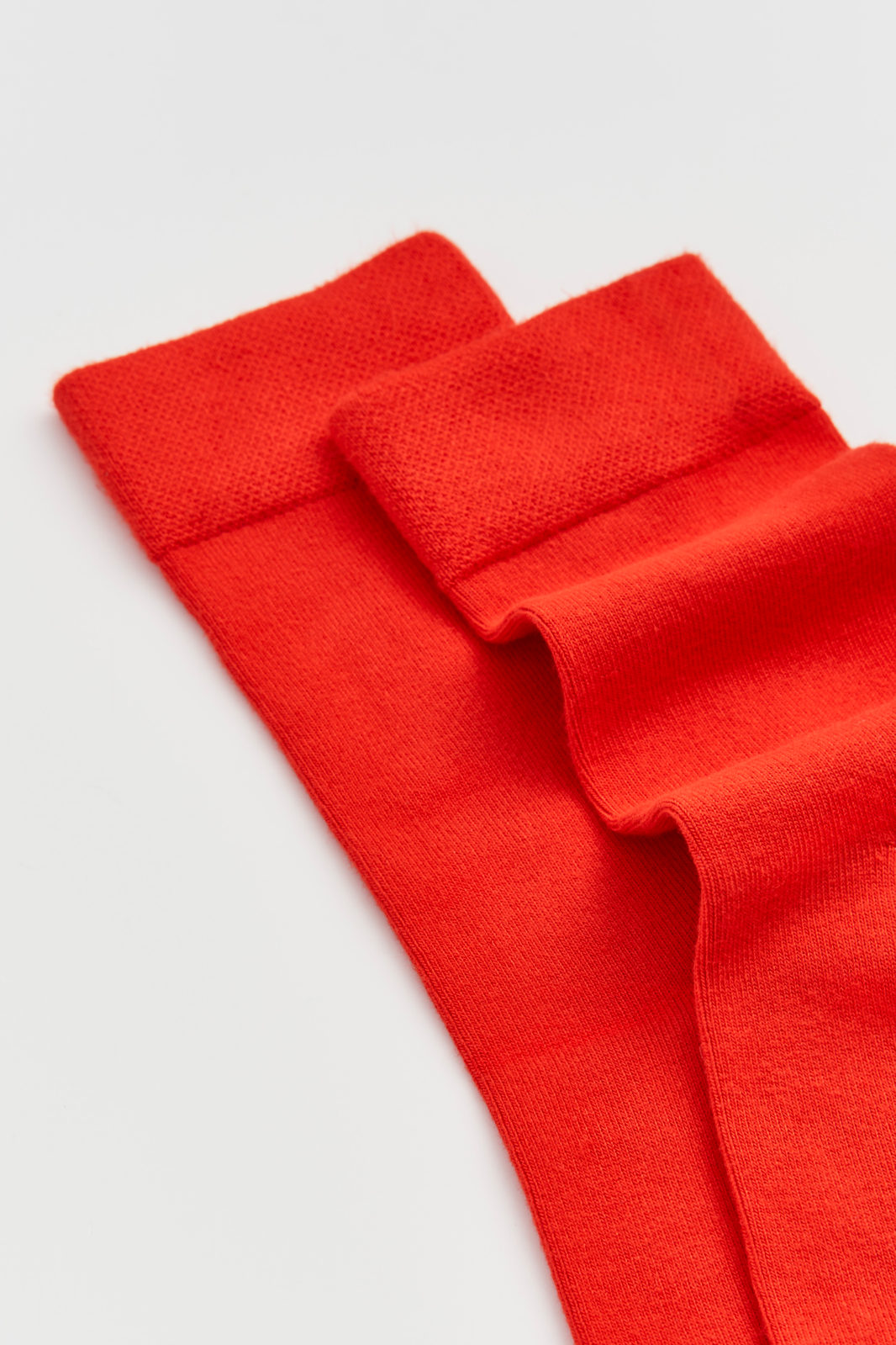 Close-up of the top of a pair of red calf-length bamboo socks on a light grey background