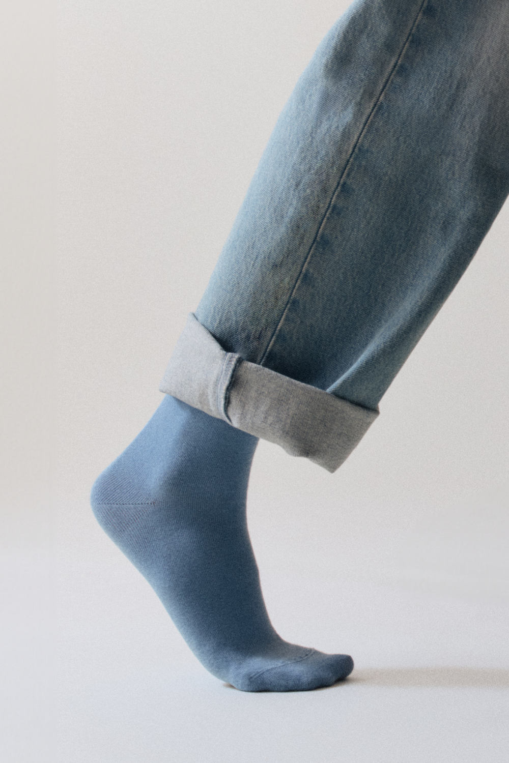 Person wearing blue jeans with rolled-up cuffs and matching light blue bamboo calf length socks on a neutral background