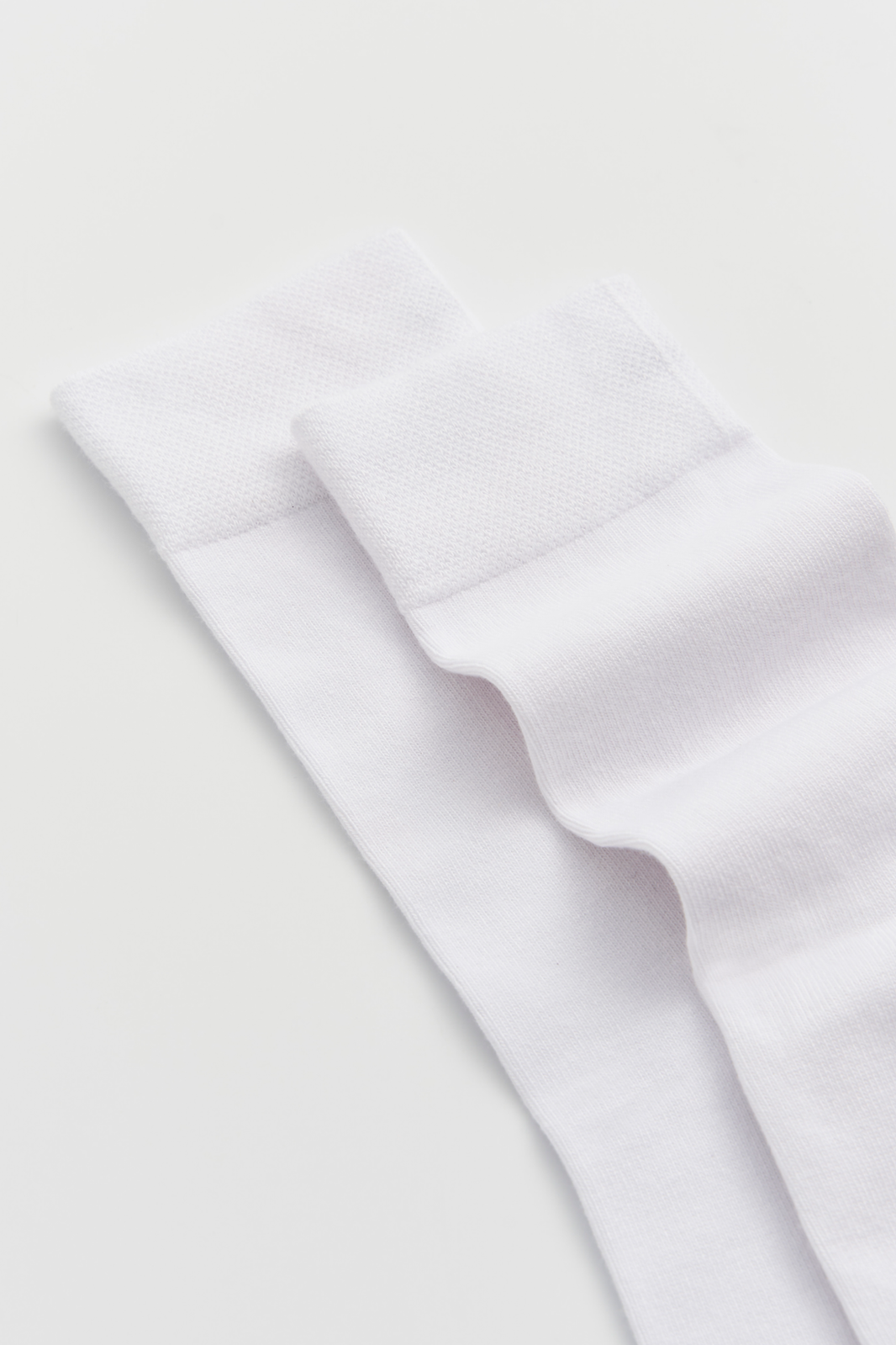 Close-up of the top of a pair of white calf-length bamboo socks on a light grey background