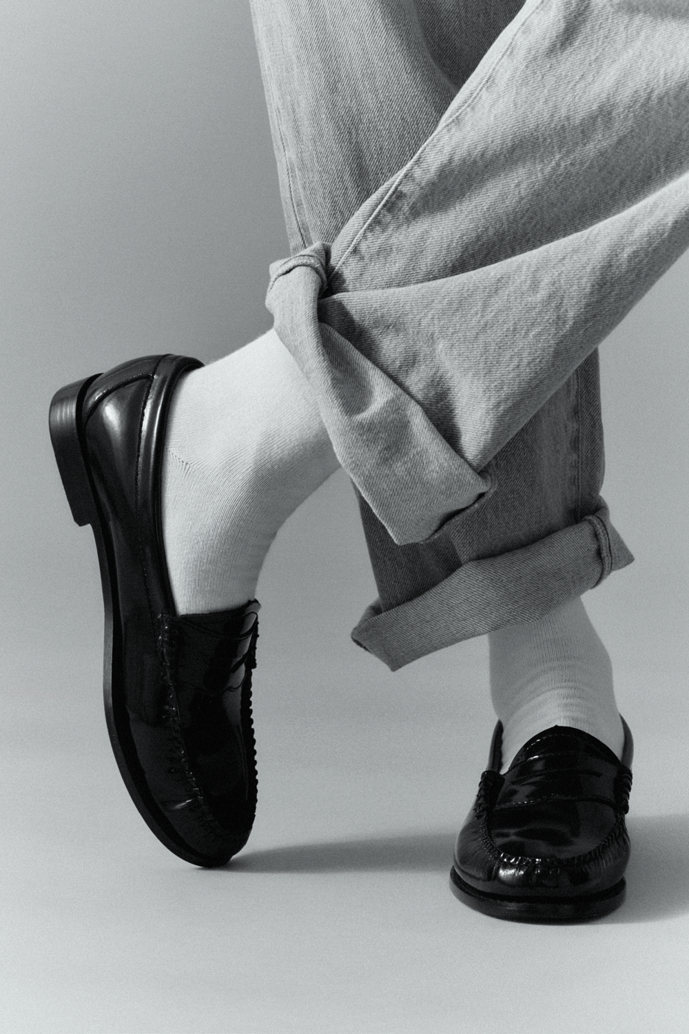 Person wearing white calf length bamboo socks, black shoes and light grey jeans on a plain background