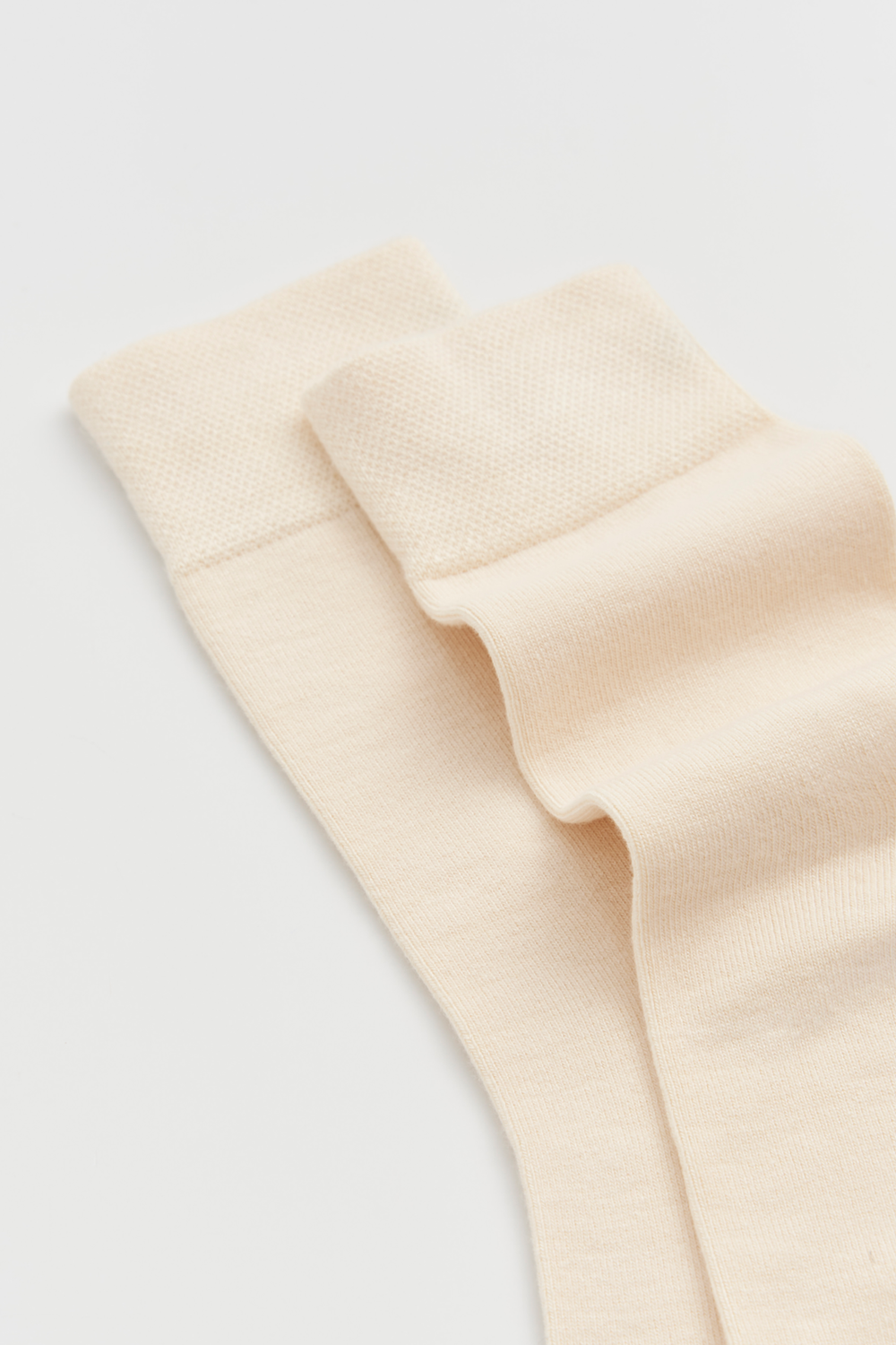 Close-up of a pair of cream calf-length bamboo socks on a light grey background