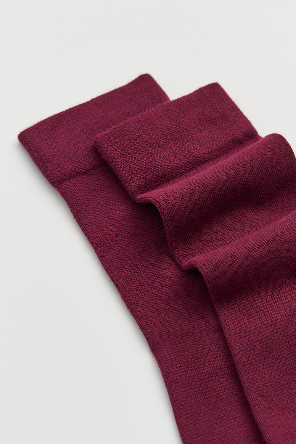 Close-up of the top of a pair of burgundy calf-length bamboo socks on a light grey background