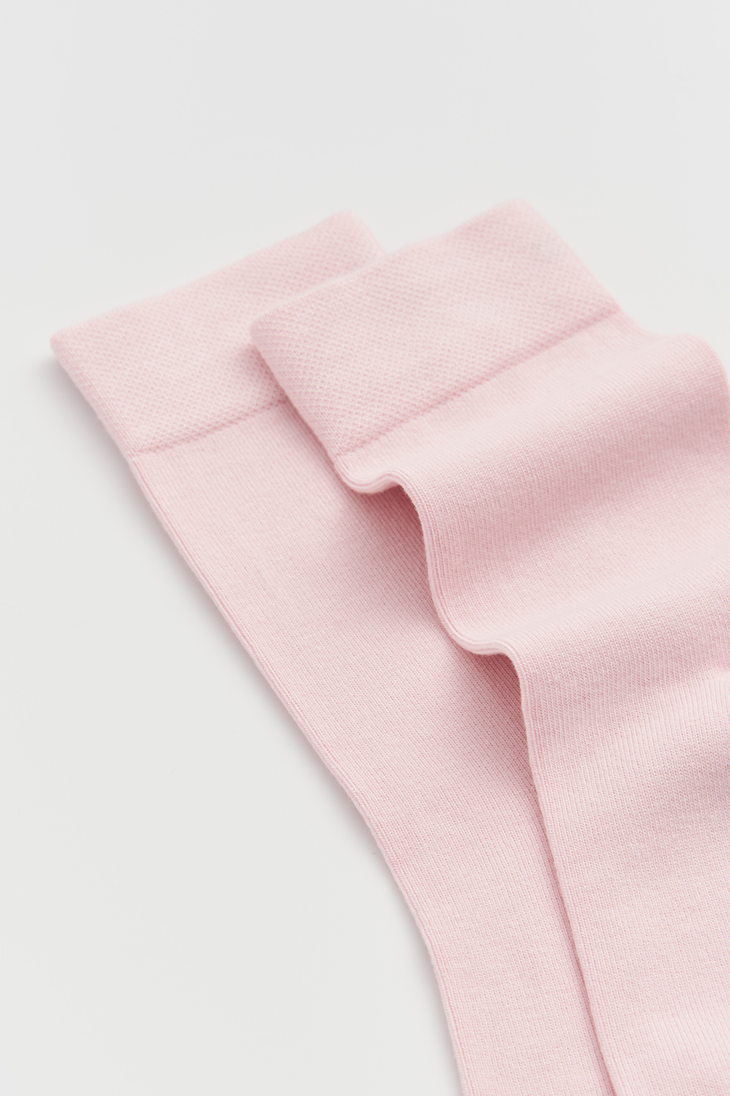 Close-up of the top of a pair of pale pink calf-length bamboo socks on a light grey background