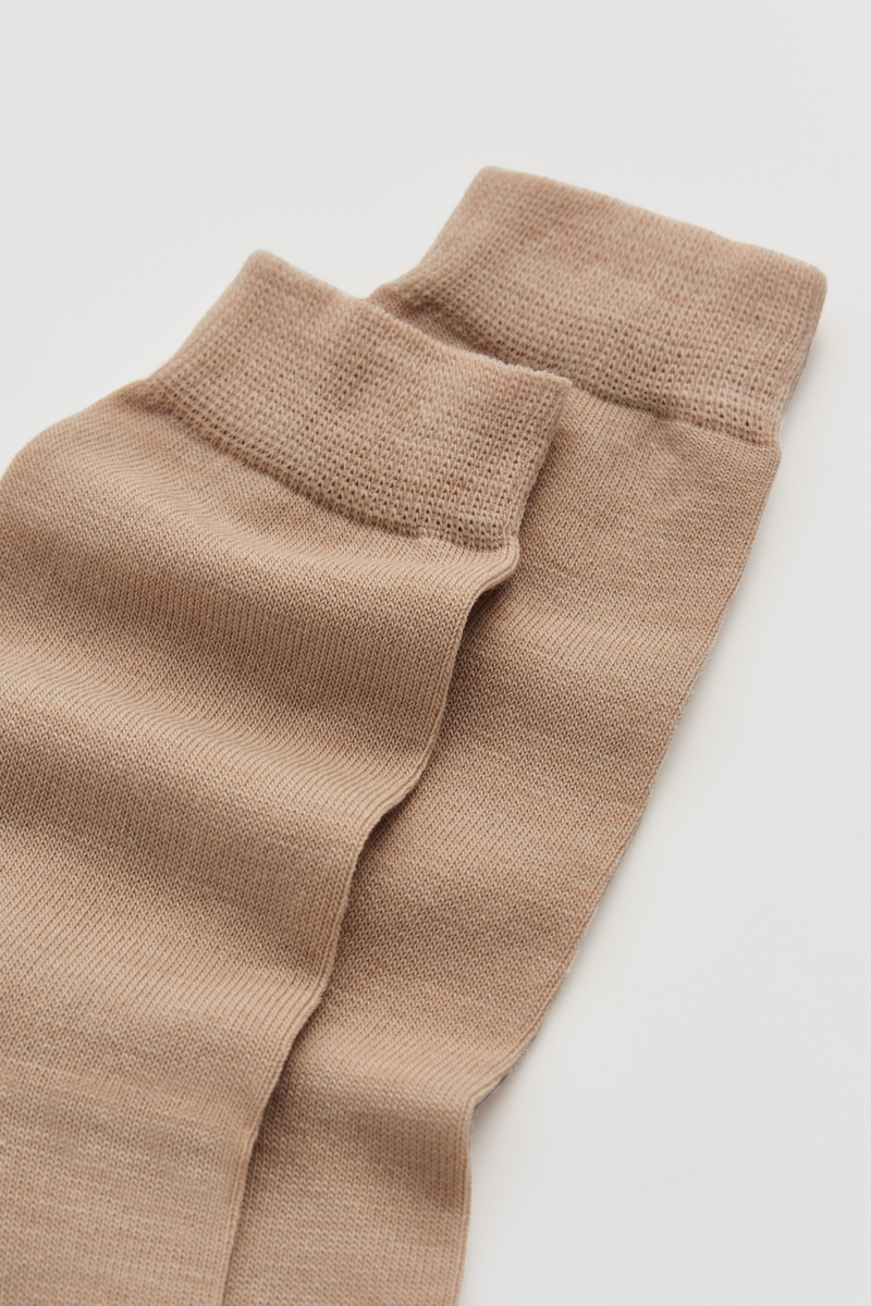 Pair of beige calf-length merino socks on a white background