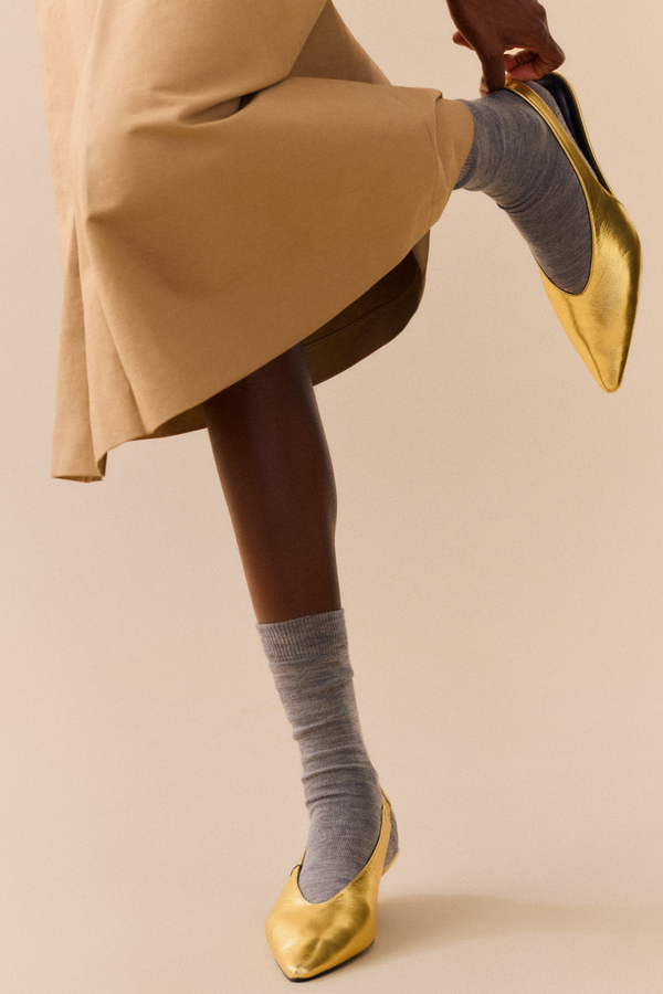 Person wearing gold shoes and mid-grey calf length merino socks on a beige background