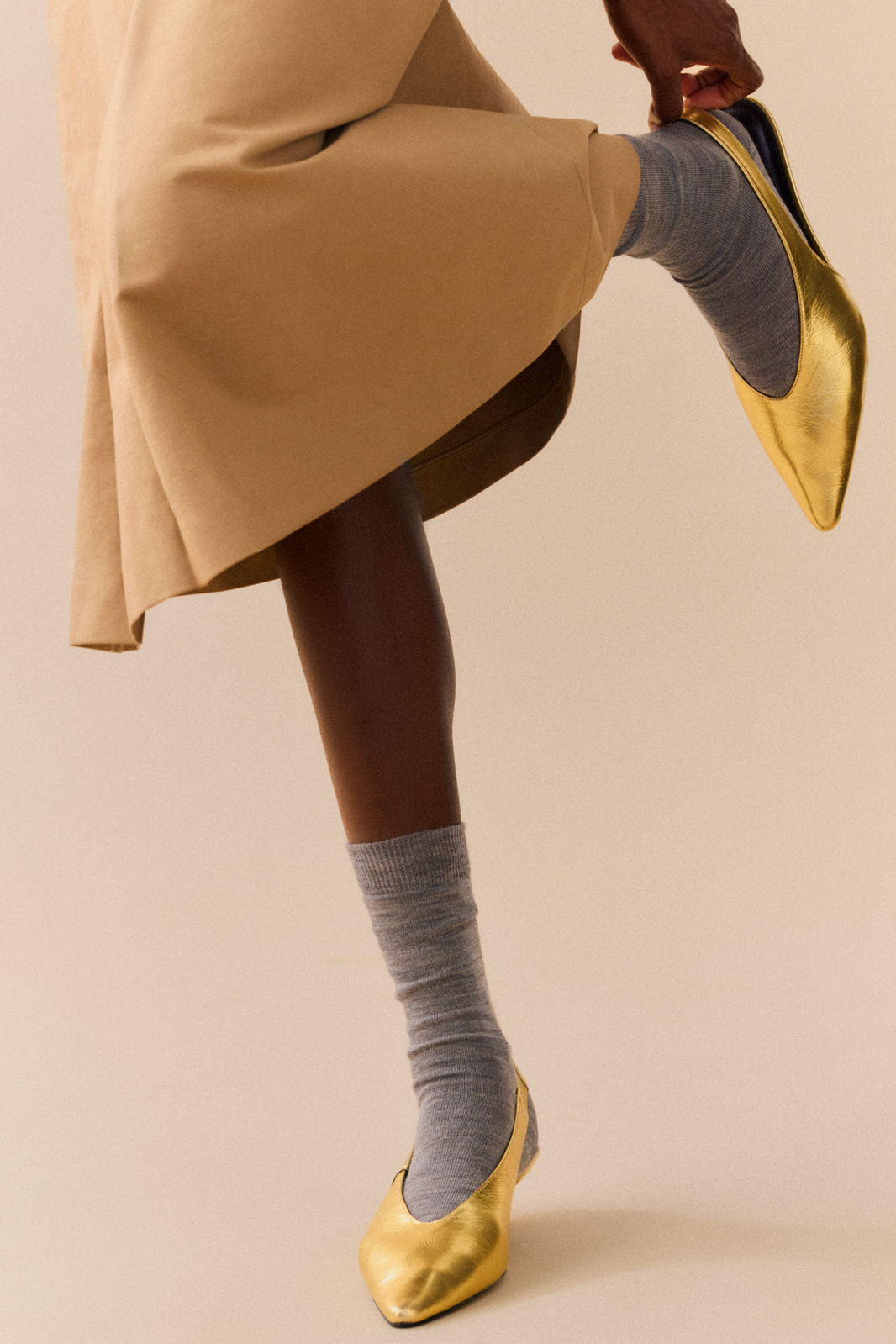Person wearing grey merino calf length socks and gold shoes on a plain background