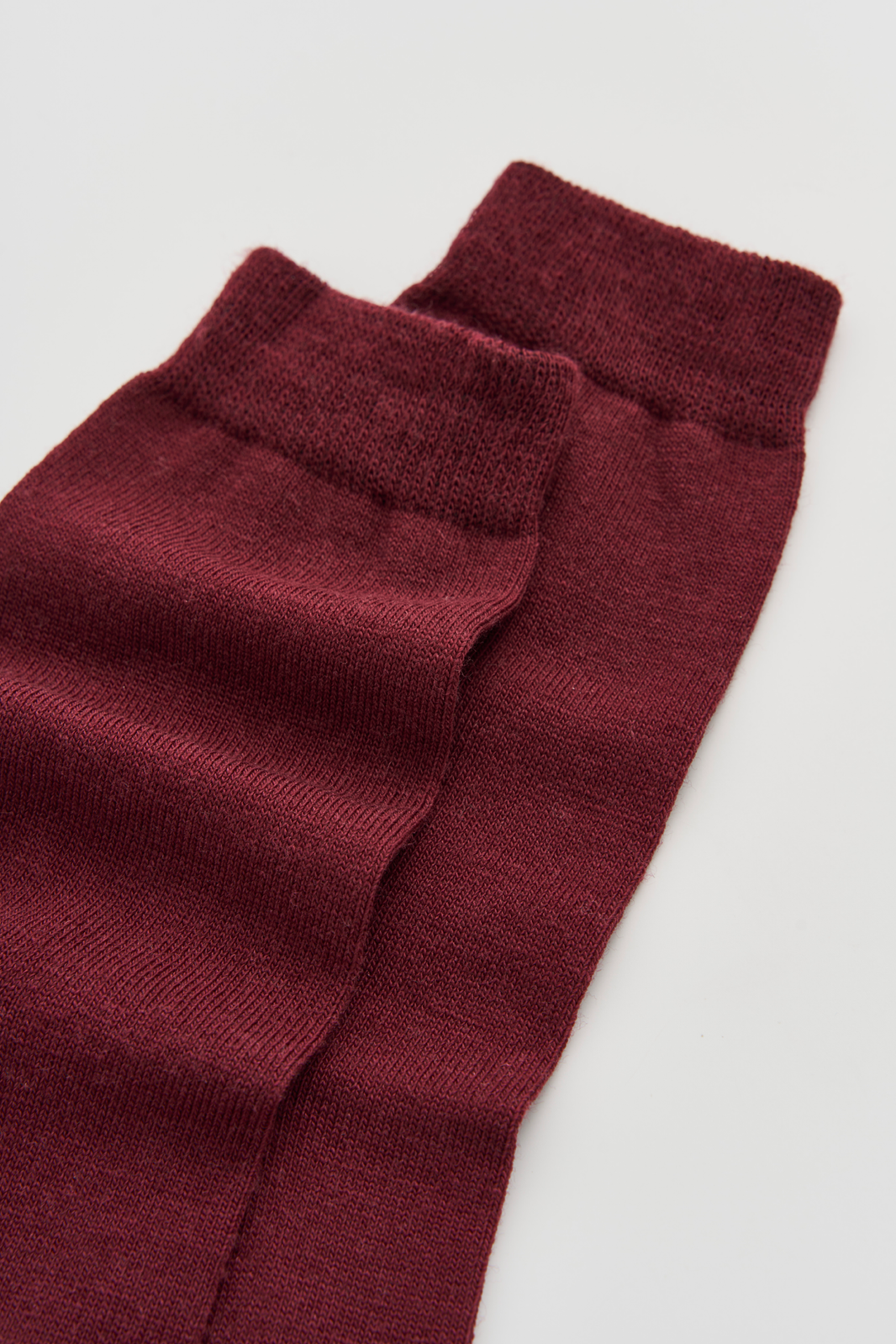 Close-up of the top of a pair of burgundy calf-length merino socks on a light grey background