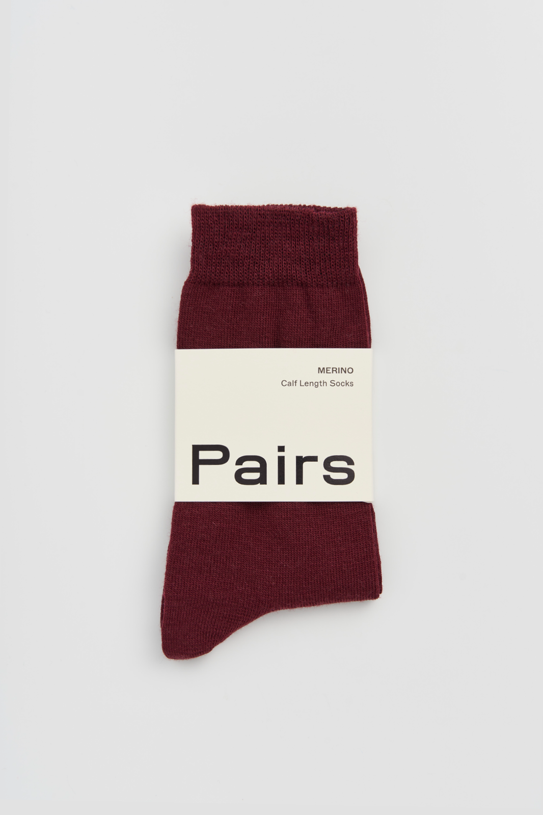 Burgundy calf-length merino sock with a 'Pairs' packaging band on a light grey background