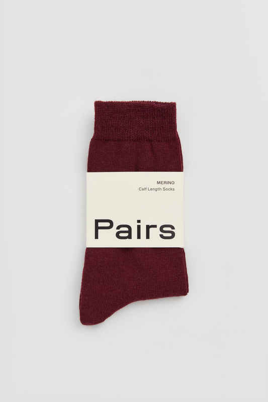 Burgundy calf-length merino sock with a 'Pairs' packaging band on a light grey background