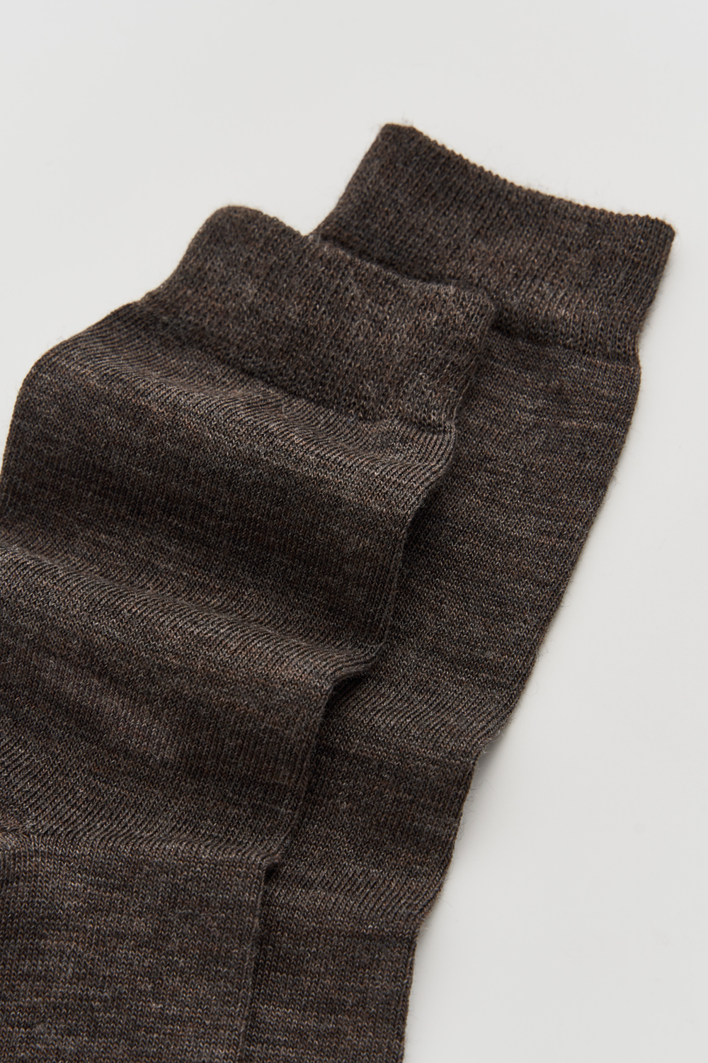 Close-up of the top of a pair of dark brown calf-length merino socks on a light grey background