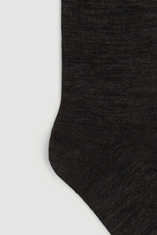 Close-up of the heel of a dark brown calf length merino sock on a white background