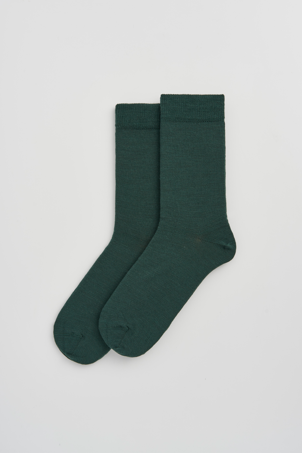 Pair of dark green calf-length merino socks on a light grey background