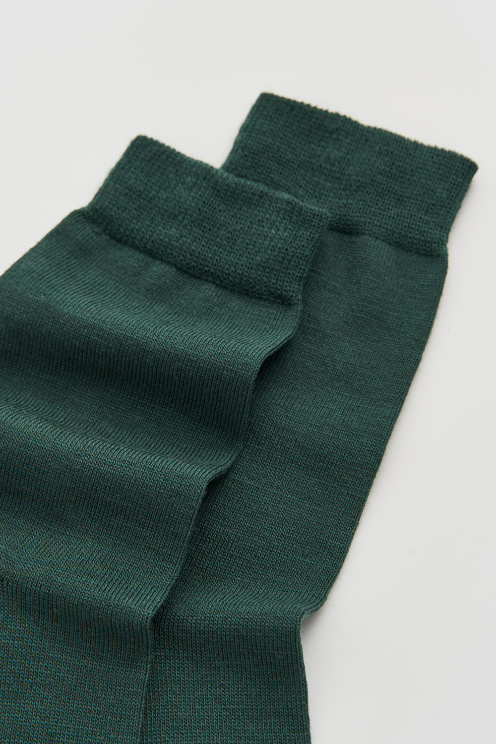 Close-up of the top of a pair of dark green calf-length merino socks on a light grey background