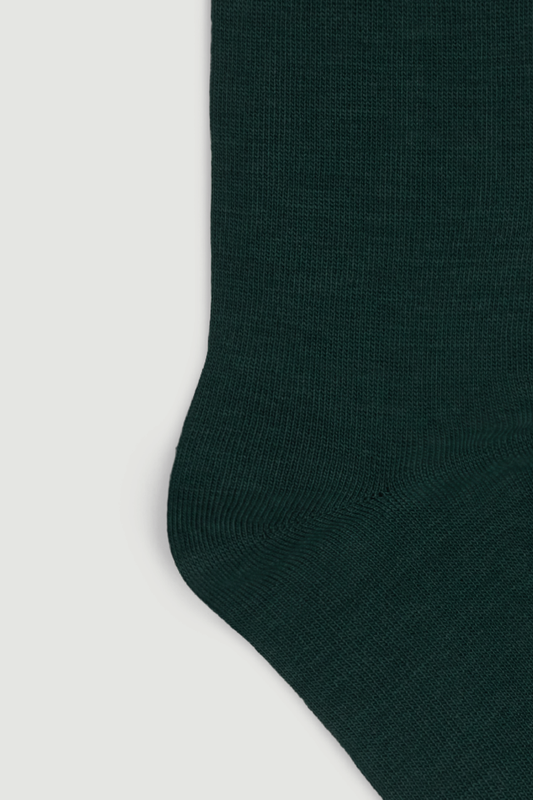 Close-up of the heel of a dark green calf length merino sock on a white background