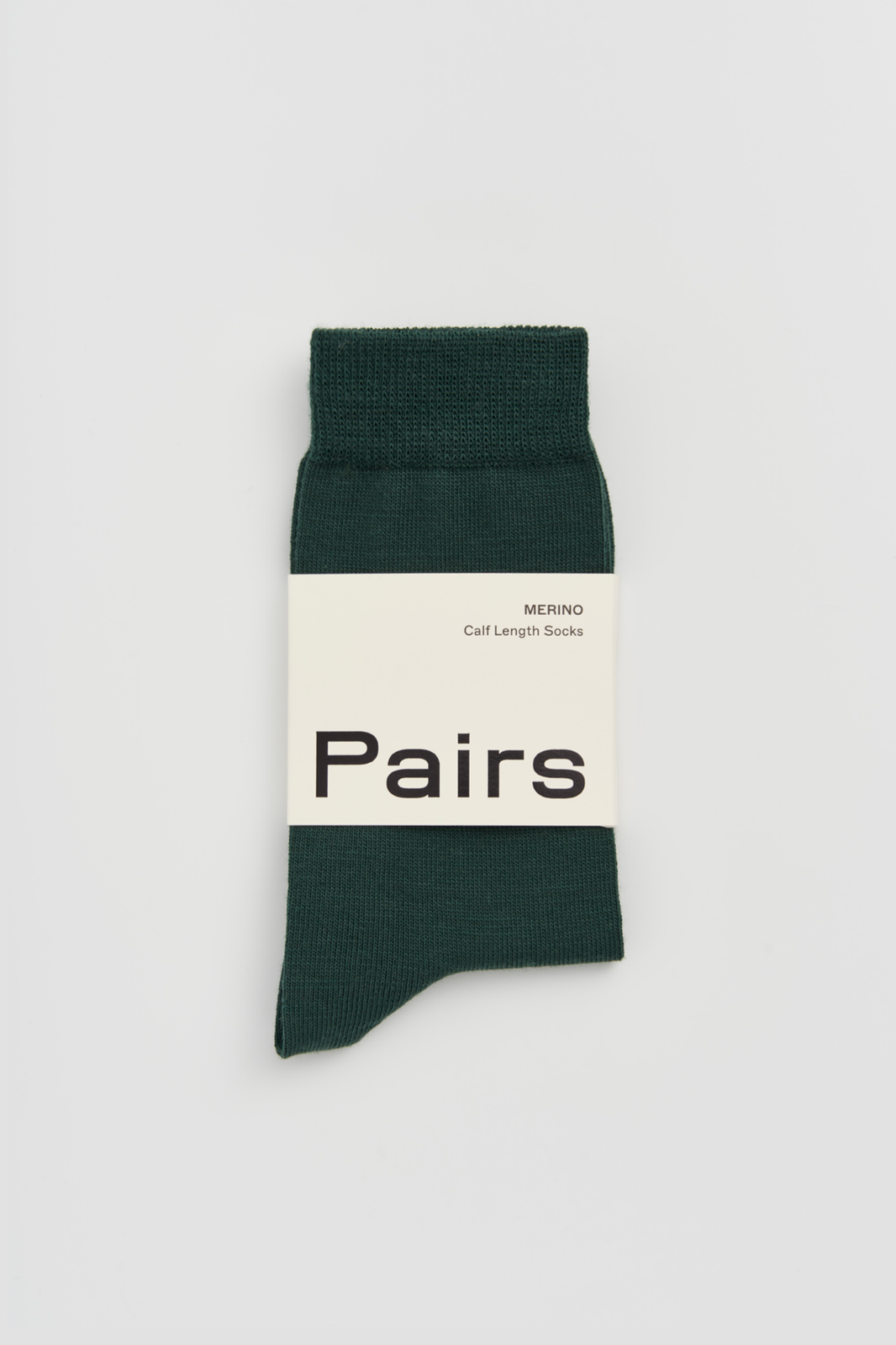 Green calf-length merino sock with a 'Pairs' packaging band on a light grey background