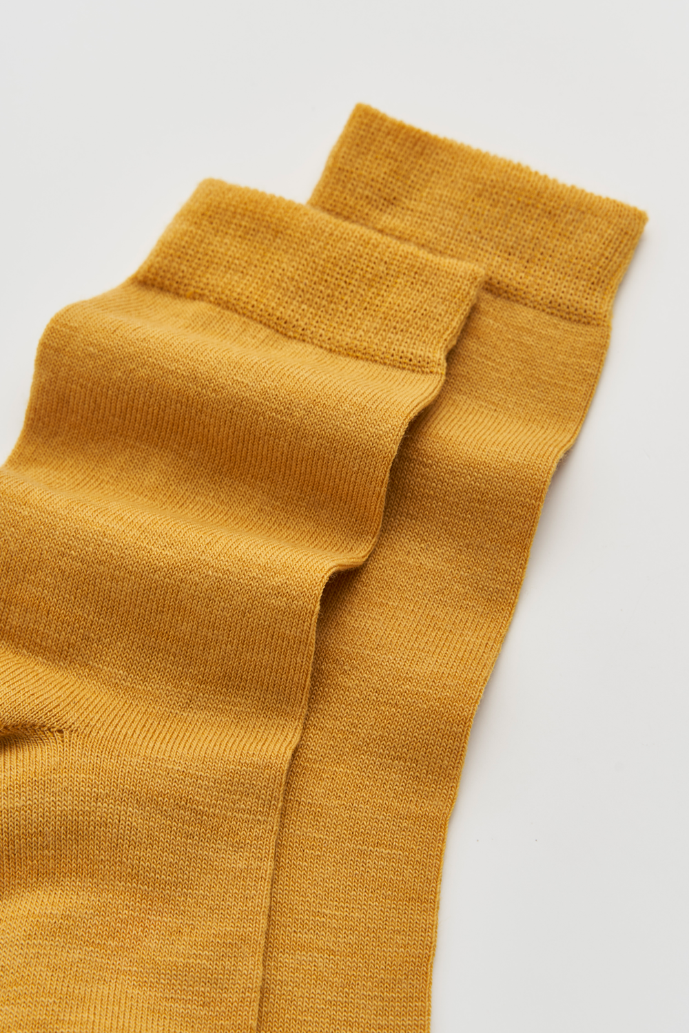 Close-up of the top of a pair of mustard yellow calf-length merino socks on a light grey background