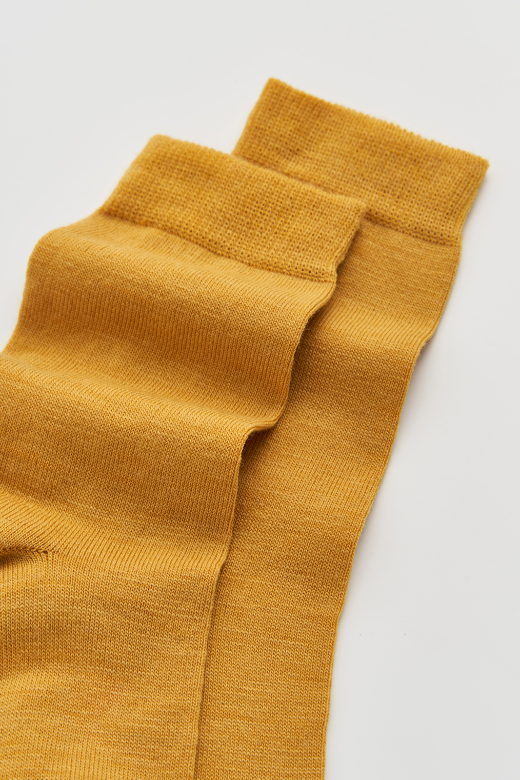 Close-up of the top of a pair of mustard yellow calf-length merino socks on a light grey background