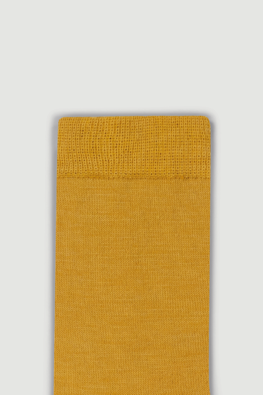 Close-up of the top of a mustard yellow calf length merino sock on a white background