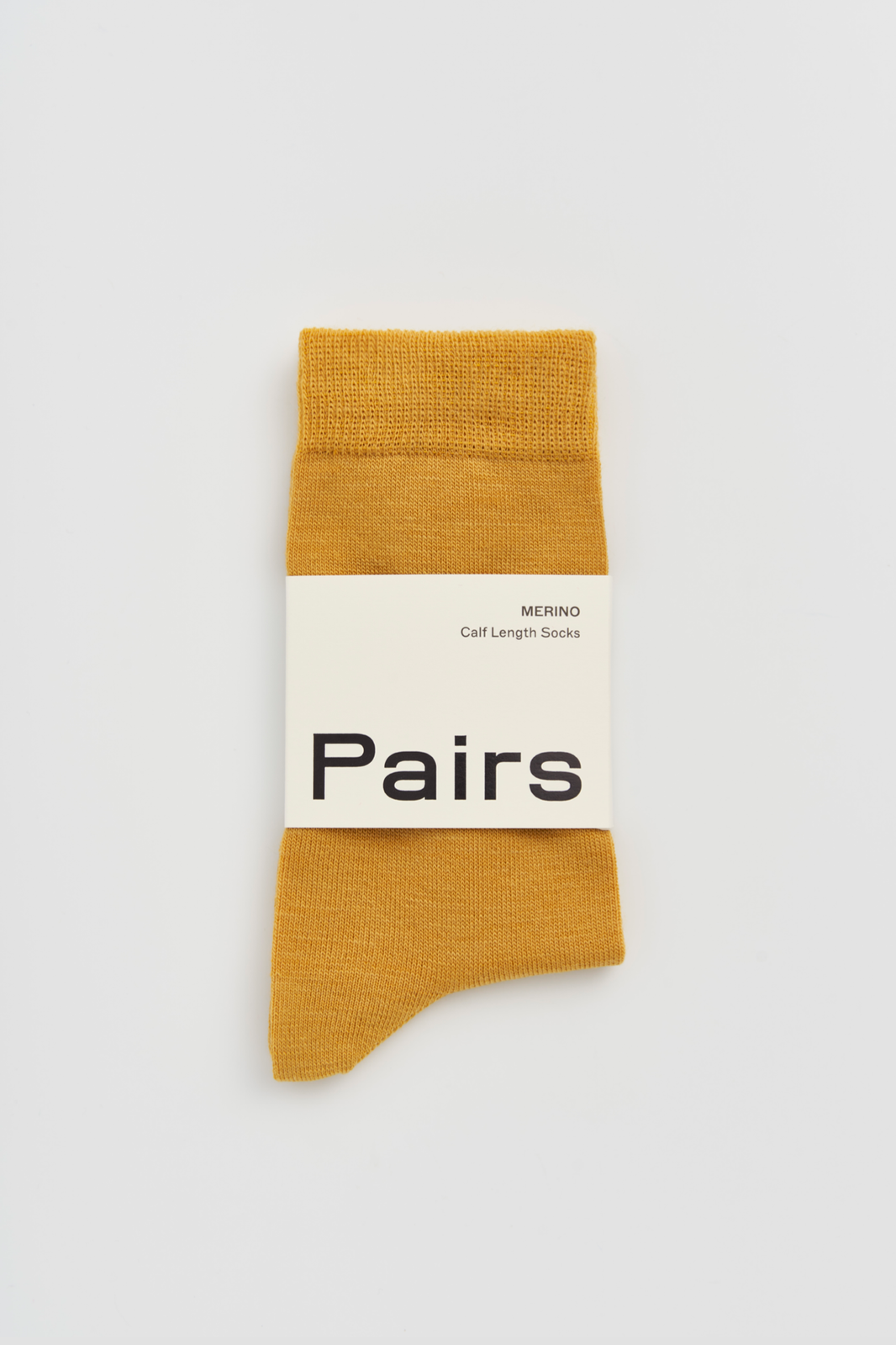 Mustard yellow calf-length merino sock with a 'Pairs' packaging band on a light grey background