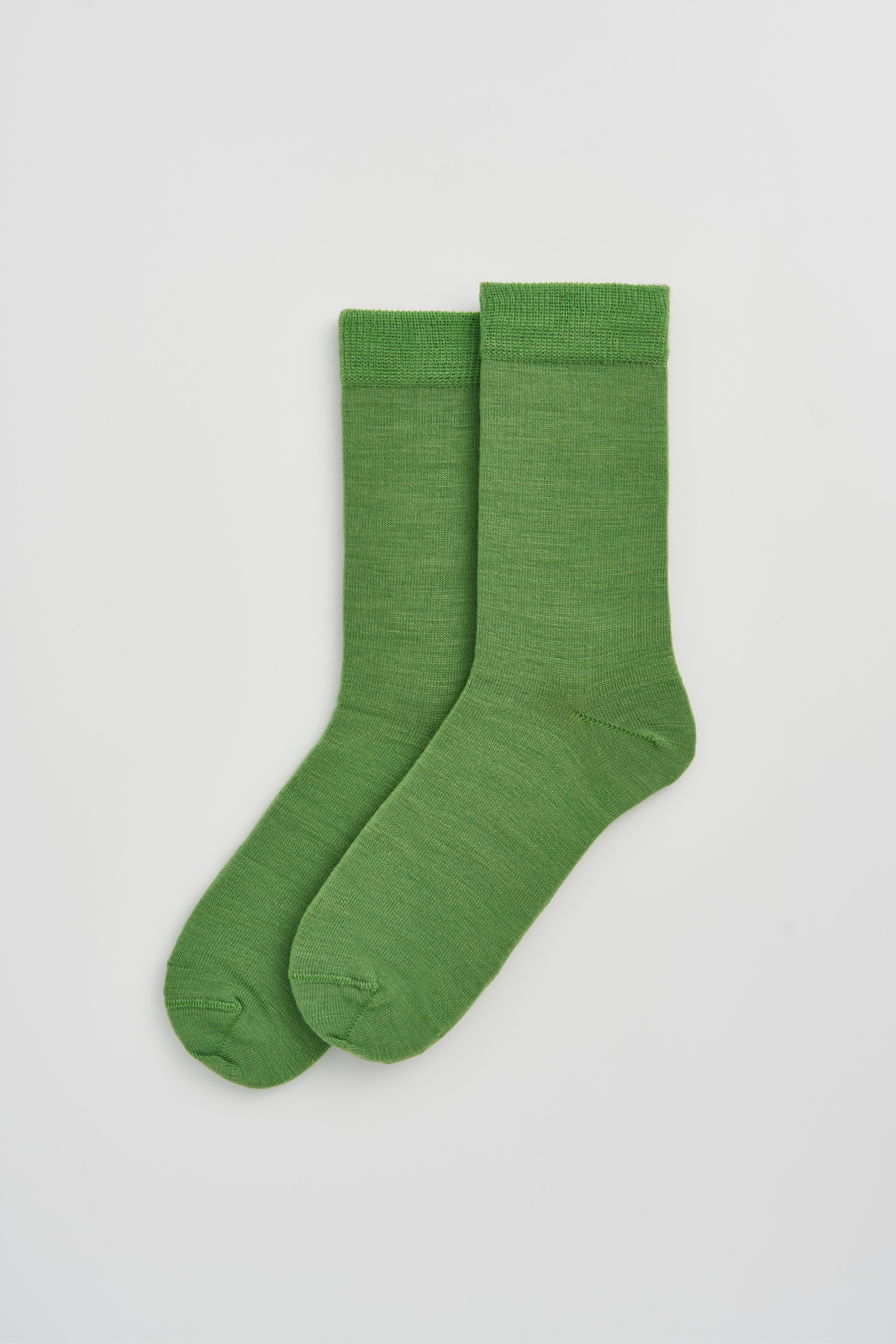 Pair of grass green calf-length merino socks on a light grey background