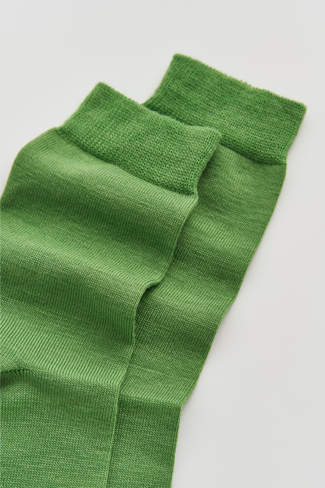 Close-up of the top of a pair of grass green calf-length merino socks on a light grey background
