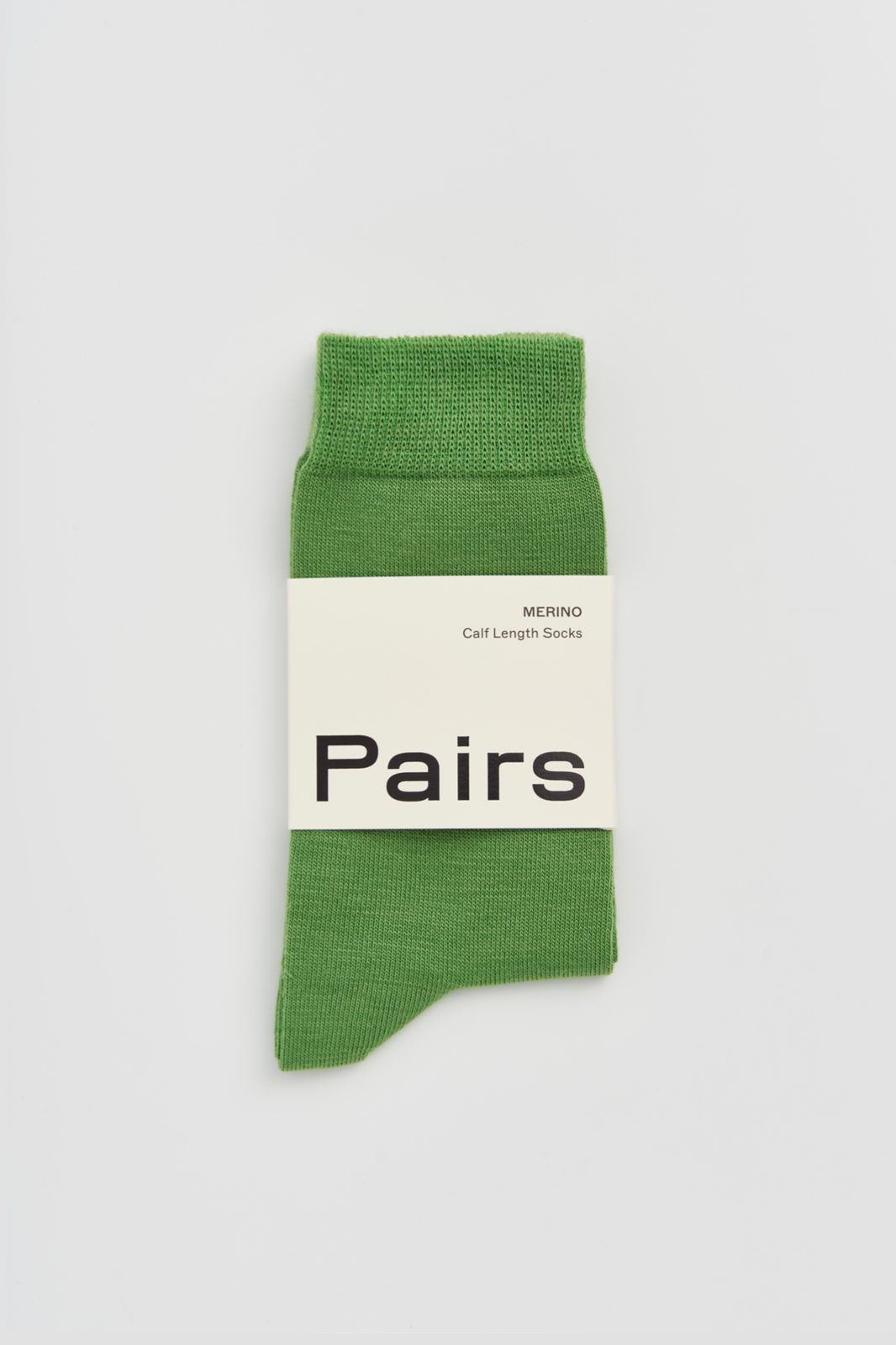 Grass green calf-length merino sock with a 'Pairs' packaging band on a light grey background