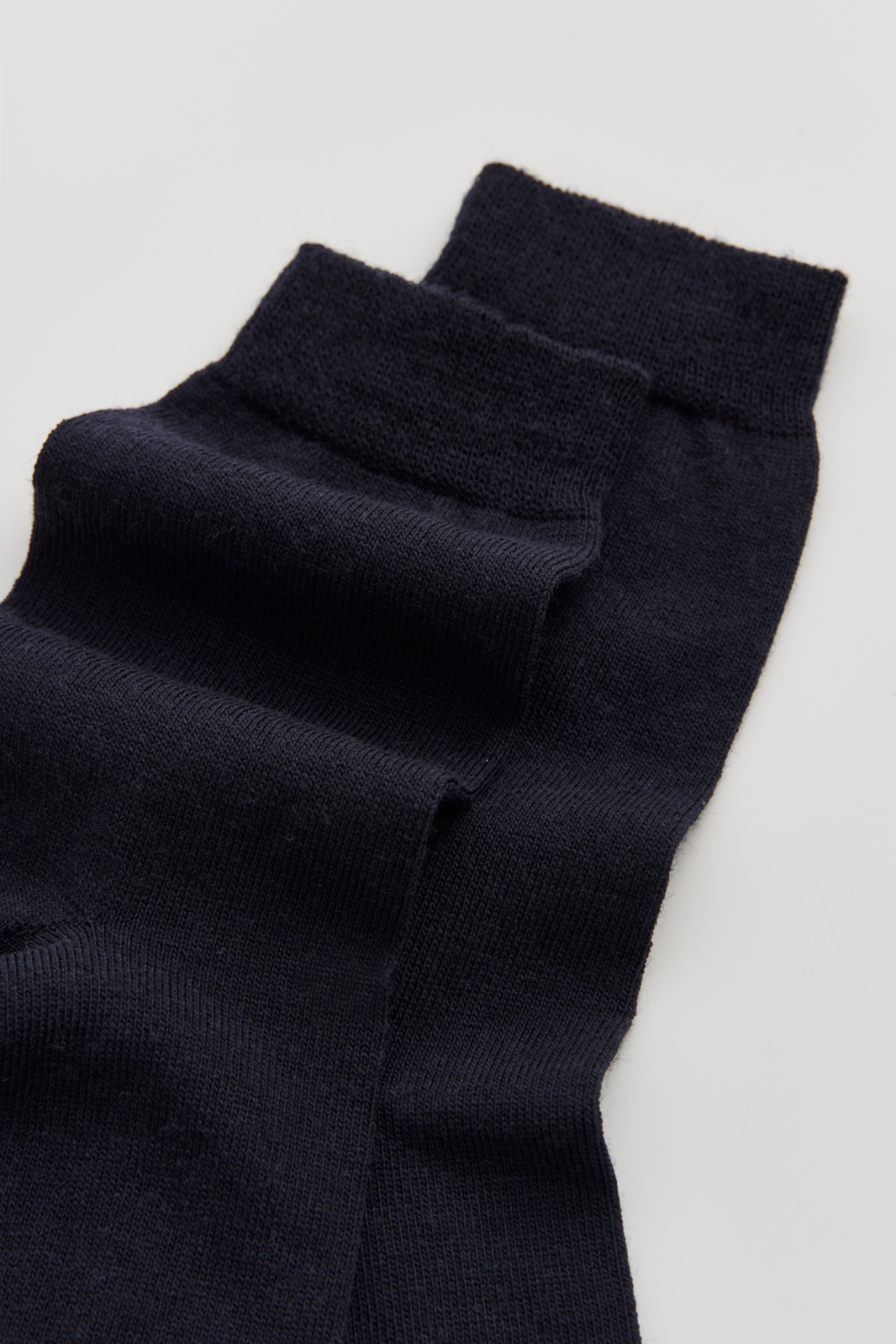 Close-up of a pair of navy calf-length merino socks on a light grey background
