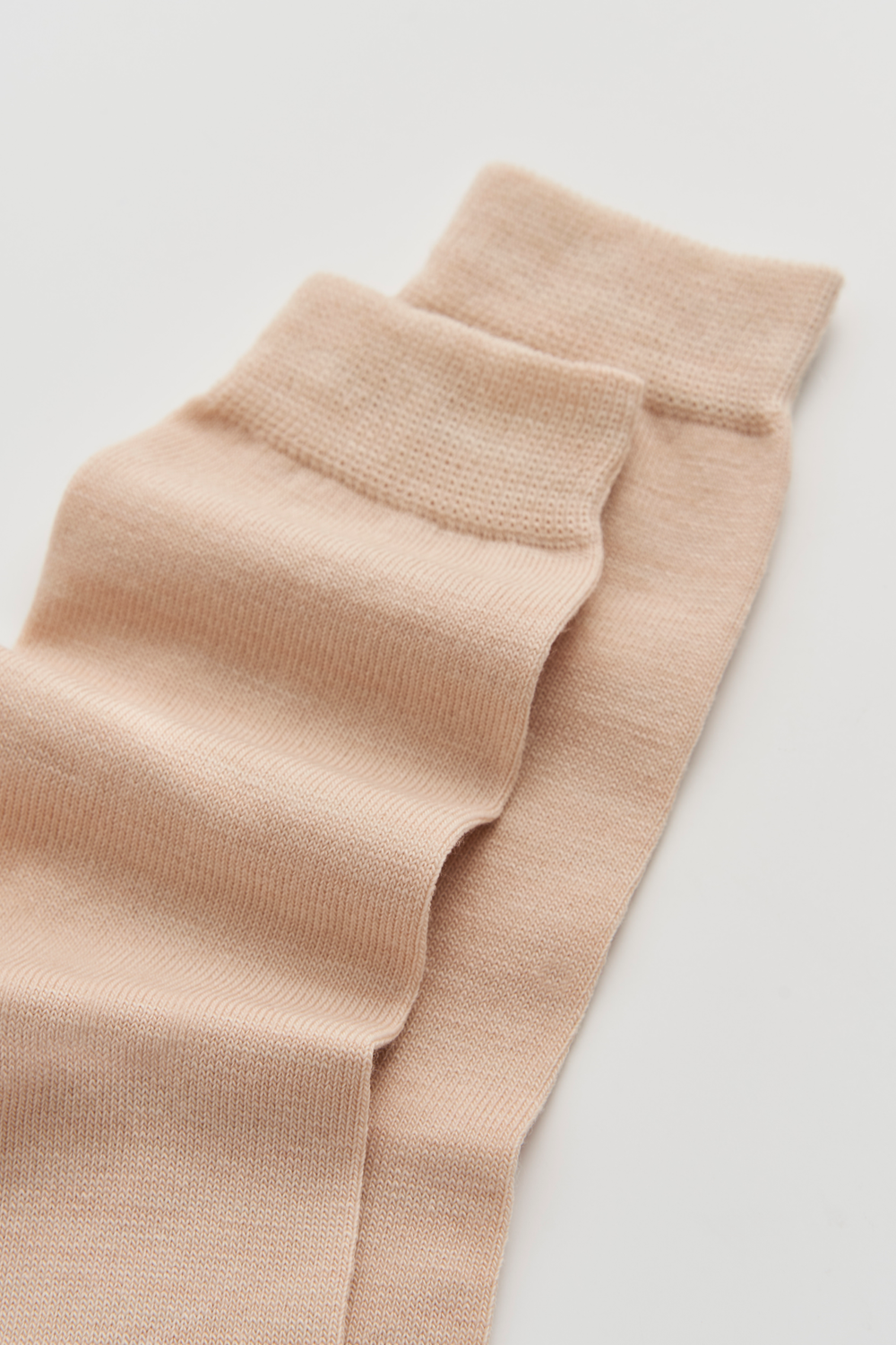 Close-up of the top of a pair of light beige calf-length merino socks on a light grey background