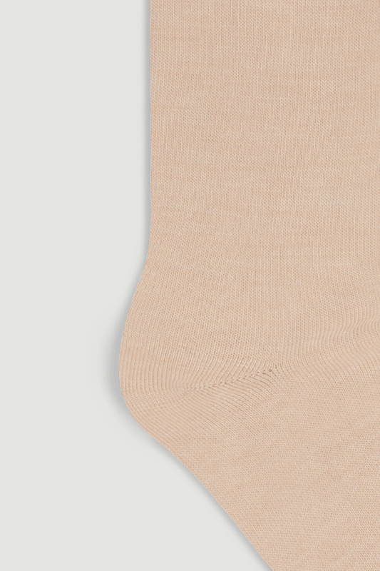 Close-up of the heel of a beige calf length merino sock on a white background