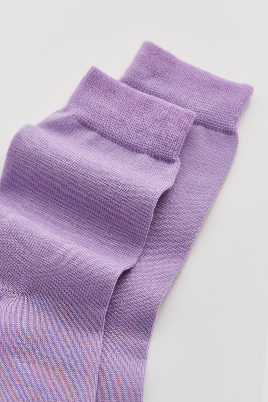 Close-up of the top of a pair of lilac calf-length merino socks on a light grey background