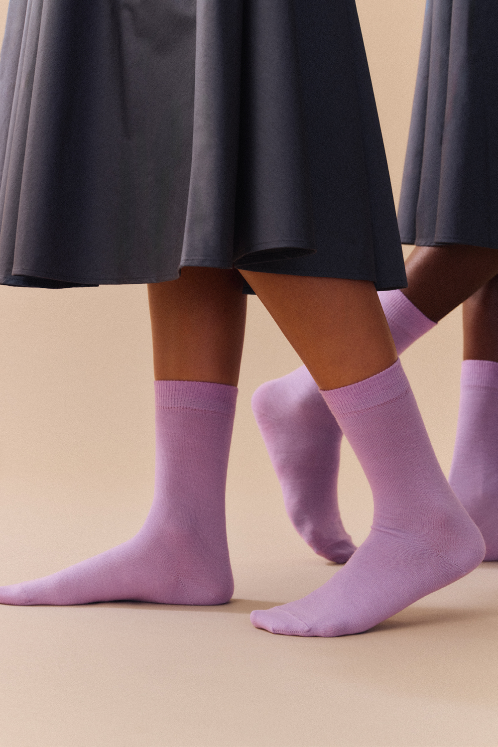 Lilac calf length merino socks worn with a dark skirt on a beige background