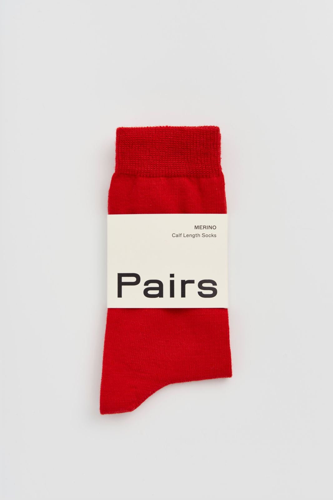 Red calf-length merino sock with a 'Pairs' packaging band on a light grey background