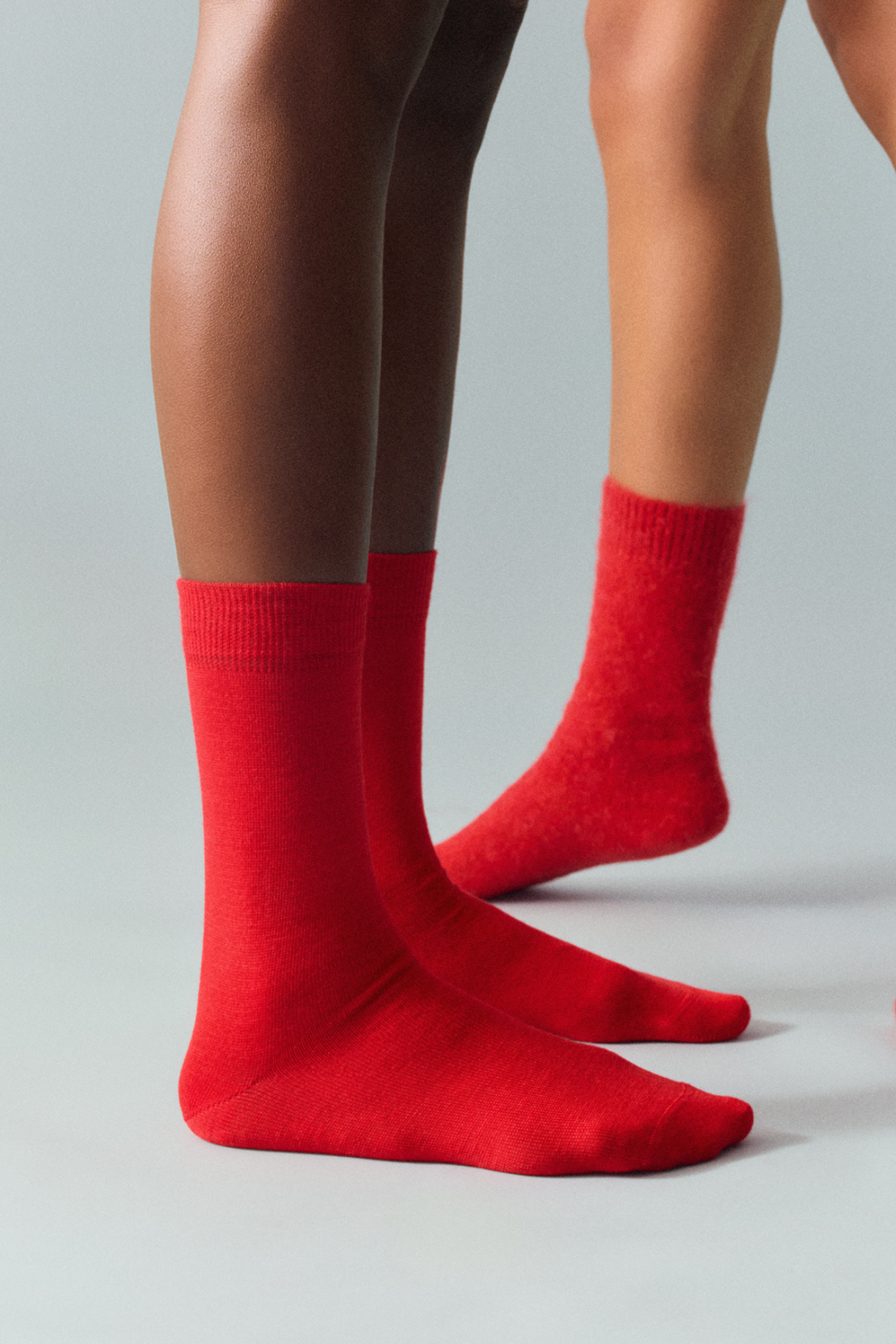Bright red calf length merino socks worn by a person on a grey background