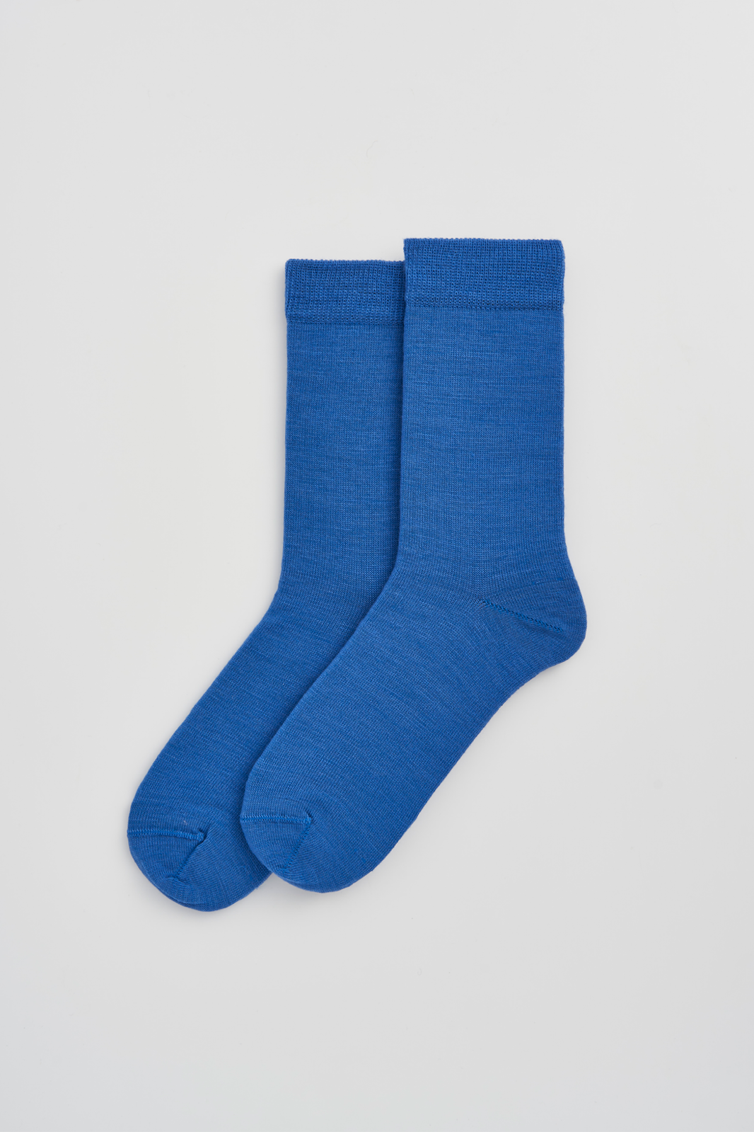 Pair of bright blue calf-length merino socks on a light grey background