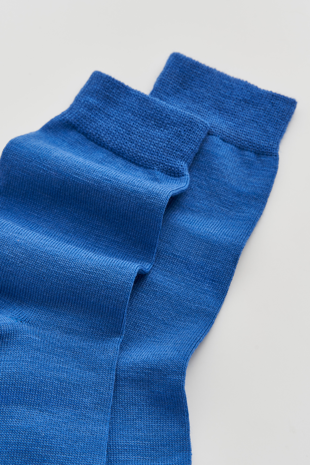 Close-up of the top of a pair of bright blue calf-length merino socks on a light grey background